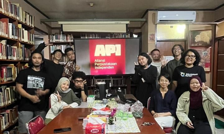 Kawan-kawan API berkumpul mengelilingi meja di sebuah perpustakaan, dengan logo API tampil di layar.